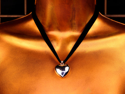 Heart-shaped bell pendant on a black velvet cord against a gold background