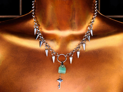 Necklace with spikes and a green pendant on a bronze surface