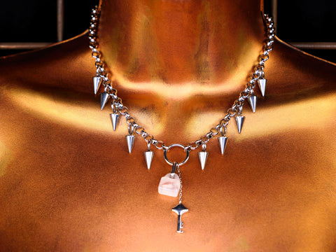 Silver necklace with spike-like beads and a central rose quartz pendant on a bronze surface